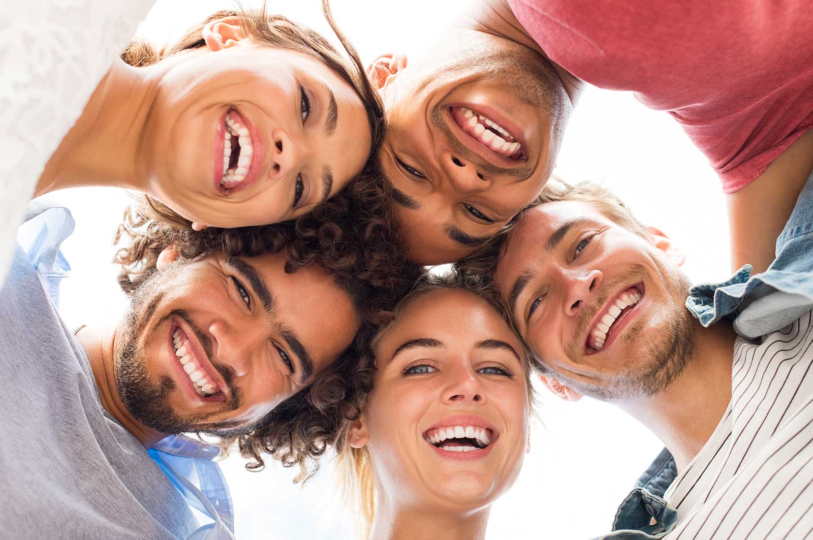 Five people with bright white smiles huddle in a hug